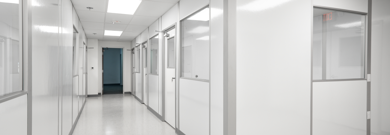 A clean, well-lit modular cleanroom hallway with white panel walls and glass windows, designed by Allied Cleanrooms.