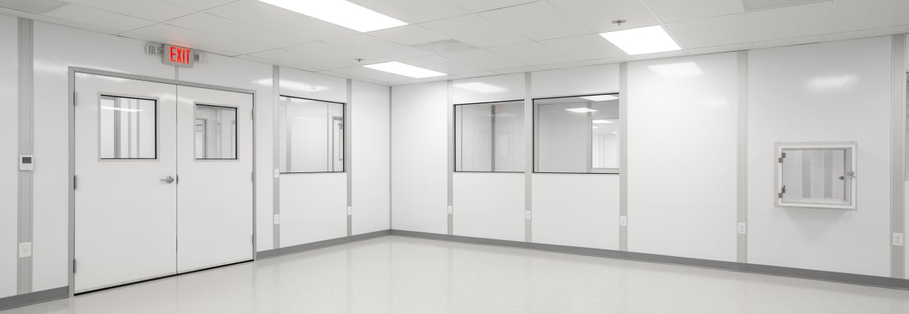 Empty cleanroom with white walls, large observation windows, bright overhead lighting, and a polished floor.