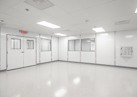 Empty cleanroom with white walls, large observation windows, bright overhead lighting, and a polished floor.