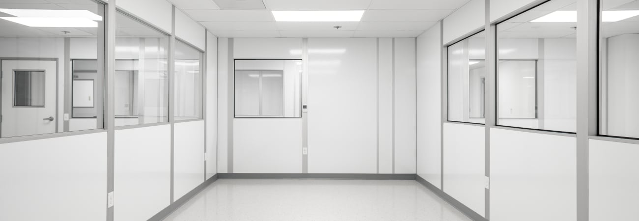 Modular cleanroom by Allied Cleanrooms featuring white panel walls, large interior windows, a polished seamless floor, and a grid ceiling with integrated lighting—designed for controlled environments in pharmaceutical or laboratory settings.