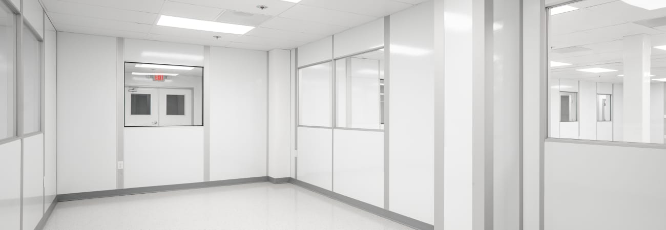 Interior of a cleanroom with white walls, bright overhead lighting, large windows, and sealed doors, showcasing a sterile and controlled environment designed for industries like pharmaceuticals and electronics manufacturing.