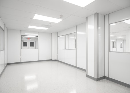 Interior of a cleanroom with white walls, bright overhead lighting, large windows, and sealed doors, showcasing a sterile and controlled environment designed for industries like pharmaceuticals and electronics manufacturing.