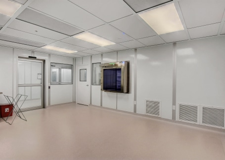 Modular cleanroom by Allied Cleanrooms with white panel walls, a smooth flooring system, and a grid ceiling with integrated lighting. The room features a pass-through chamber, multiple doors, and ventilation panels, designed for controlled environments requiring high cleanliness standards.