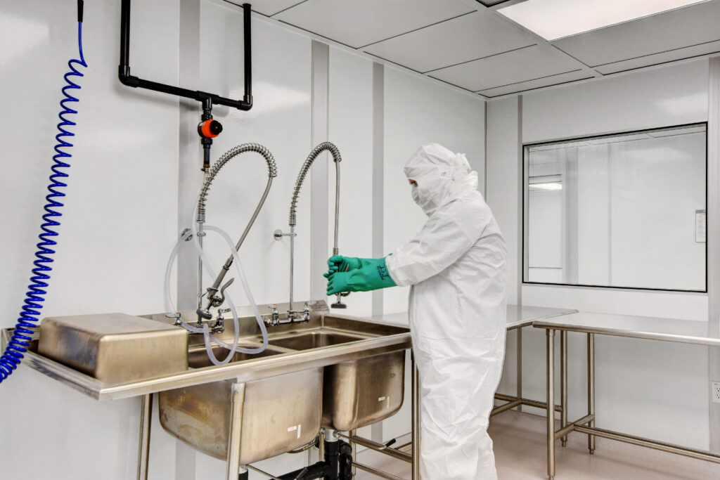 A man in a gown cleaning the sink in a cleanroom.