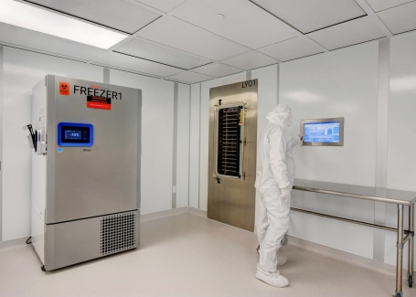 Modular cleanroom by Allied Cleanrooms featuring a technician in full gowning operating a touchscreen interface. The space includes a stainless steel lyophilizer unit labeled "LY01" and an ultra-low temperature freezer labeled "FREEZER1" set to -79°C, all housed in a clean, controlled environment with integrated lighting and seamless finishes.