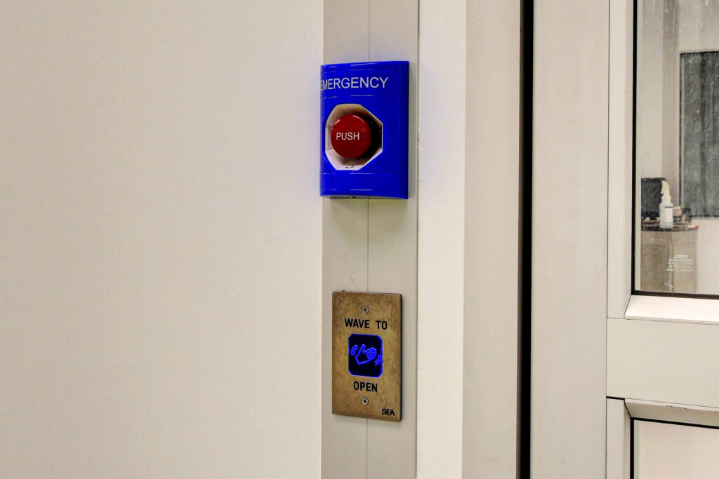 A cleanroom access point featuring a push button labeled "Emergency" and a wave-to-open sensor for hands-free operation.