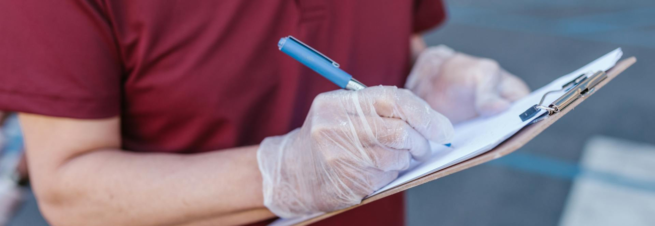 Person wearing gloves writes on a clipboard during a cleanroom testing inspection for GMP compliance for cleanrooms (at Allied Cleanrooms).