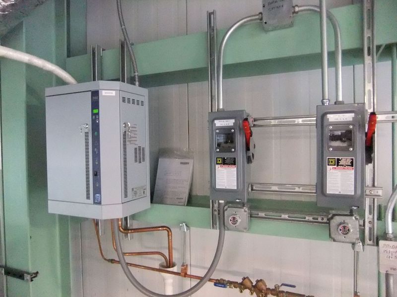 Electrical control panel and manual disconnect switches mounted on a wall with conduits and copper piping in a cleanroom utility area.