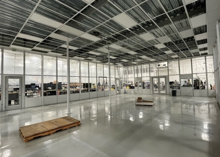 In-progress modular cleanroom by Allied Cleanrooms featuring glass wall panels, a partially installed ceiling grid, and a high-gloss epoxy floor. The cleanroom overlooks an active manufacturing area and is designed for scalable, controlled environments.