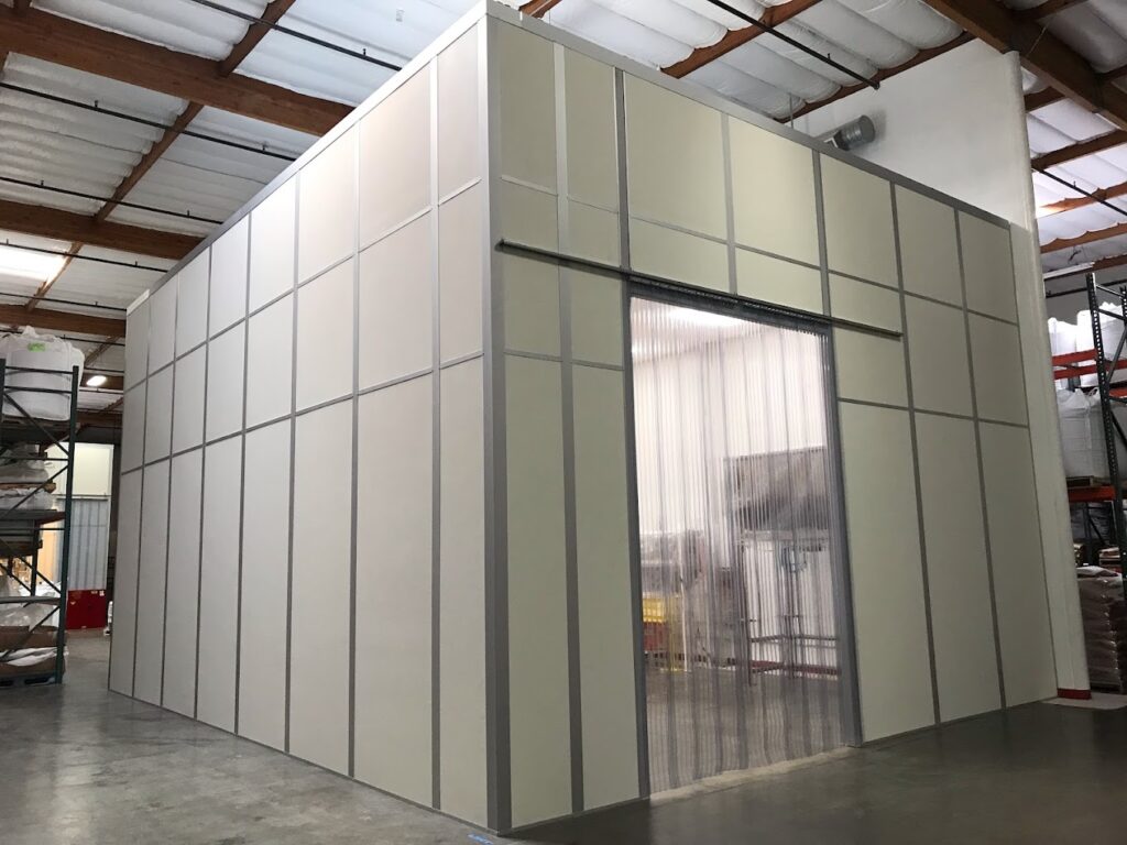 A modular packaging room with a clean and organized structure, featuring a large entryway with transparent plastic strip curtains inside a warehouse.
