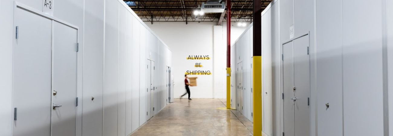 A hallway in a warehouse with multiple cleanrooms and a person walking by a wall with the sign "Always Be Shipping."