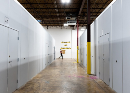 A hallway in a warehouse with multiple cleanrooms and a person walking by a wall with the sign "Always Be Shipping."