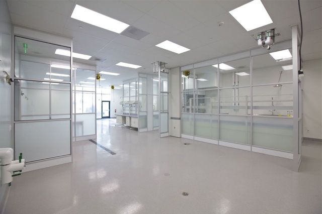 Spacious pharmaceutical cleanroom with glass partition walls, integrated workstations, and overhead utility supplies, designed for precision manufacturing and quality control.
