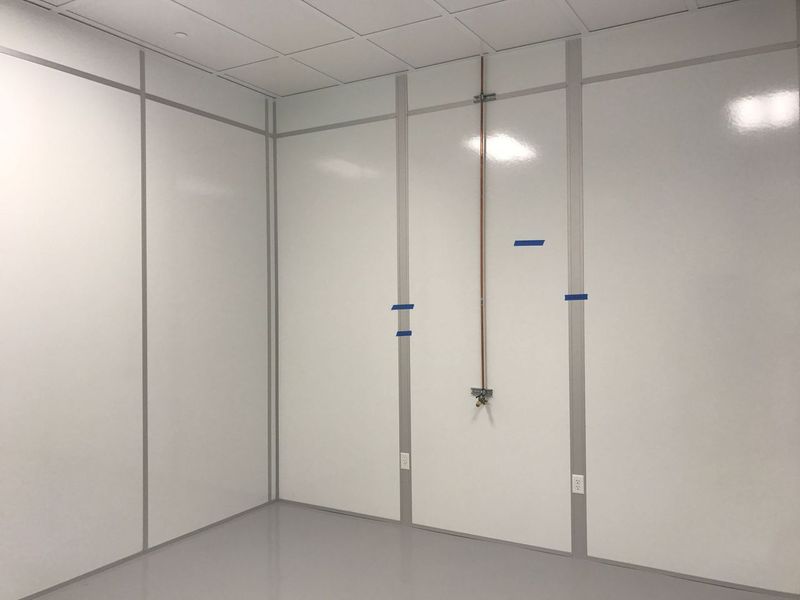 Minimalist cleanroom with white walls and glass partitions, featuring a few utility lines marked with blue tape, prepared for equipment installation.