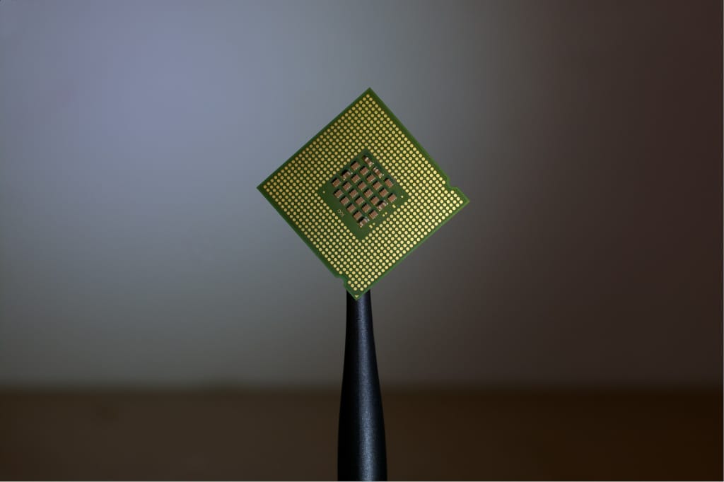 Microprocessor chip held by tweezers, representing components manufactured in semiconductor cleanrooms.