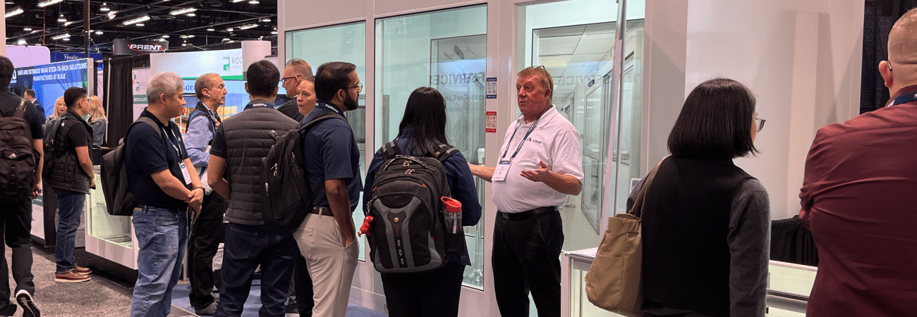 Attendees gather at the Allied Cleanrooms trade show booth, viewing a modular cleanroom structure and speaking with company representatives.
