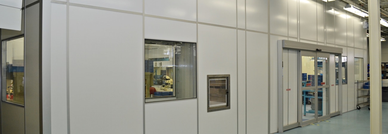 Modular cleanroom with wall panels, viewing window, pass-through chamber, and sliding door, built by Allied Cleanrooms.