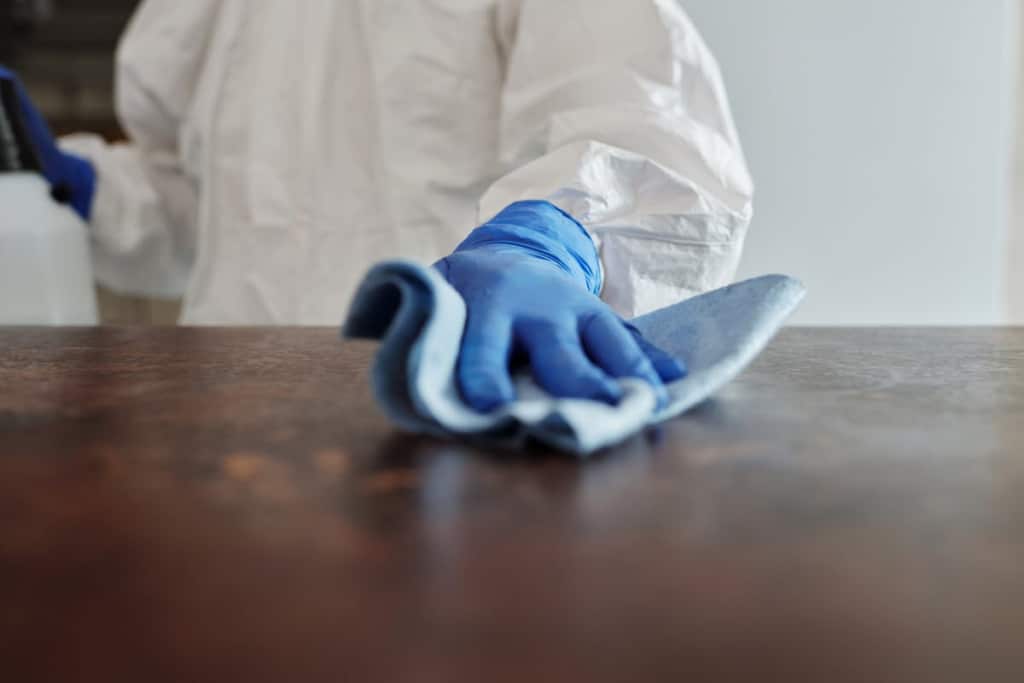 Person wearing gloves and a cleanroom suit wiping a surface as part of daily cleanroom maintenance by Allied Cleanrooms