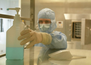 Cleanroom technician following cleanroom gowning procedures with gloves, mask, and full protective suit in a controlled environment by Allied Cleanrooms